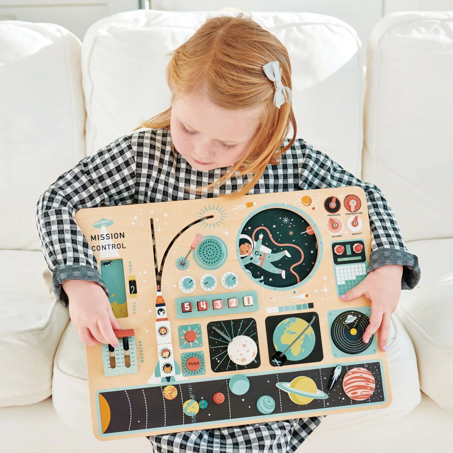Child holding a space-themed activity board on a white couch