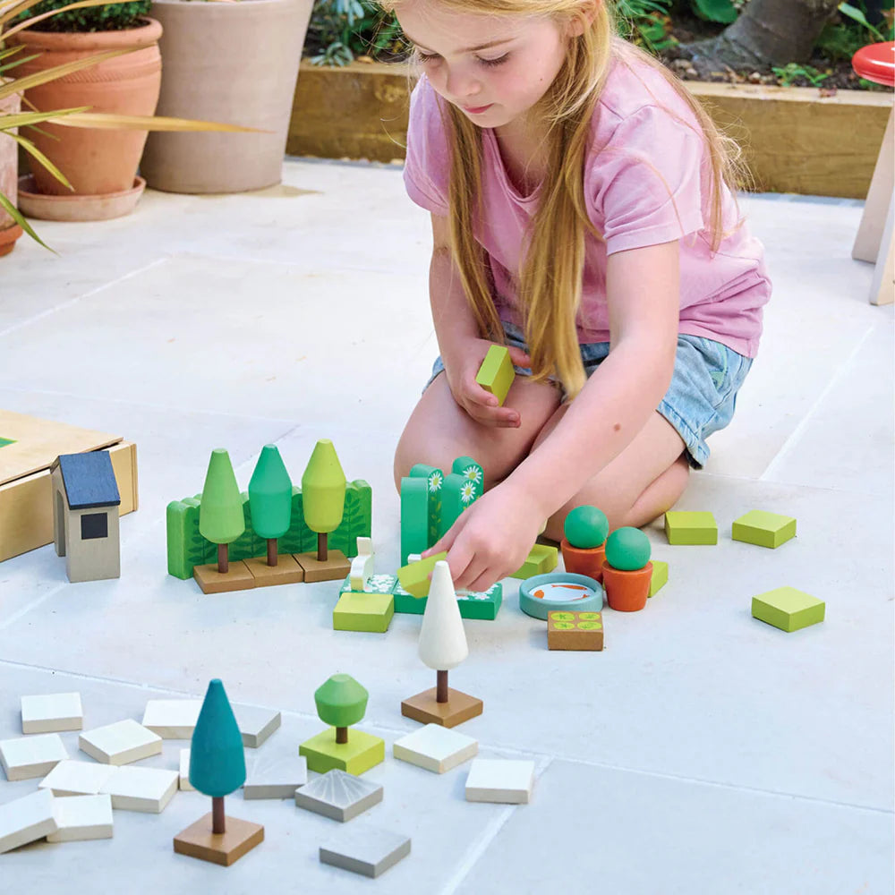 Child playing with wooden blocks shaped like trees and buildings on a light surface.