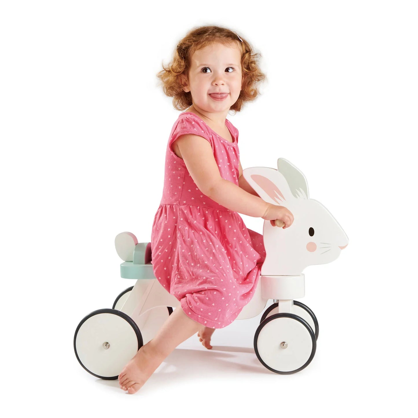 Child in a pink dress riding a white toy horse with a smiling expression on a white background