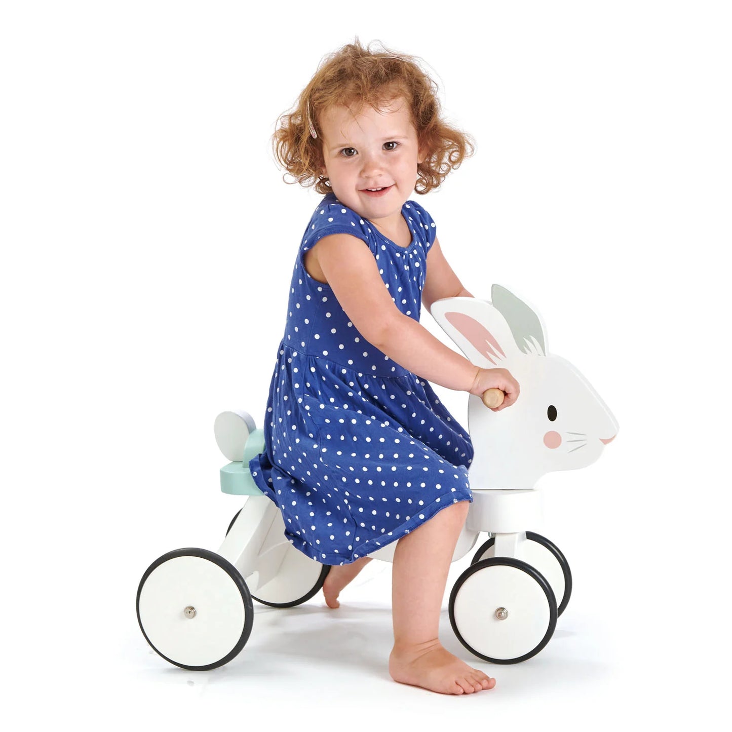 Child in a blue dress riding a white toy horse with rabbit ears on a white background