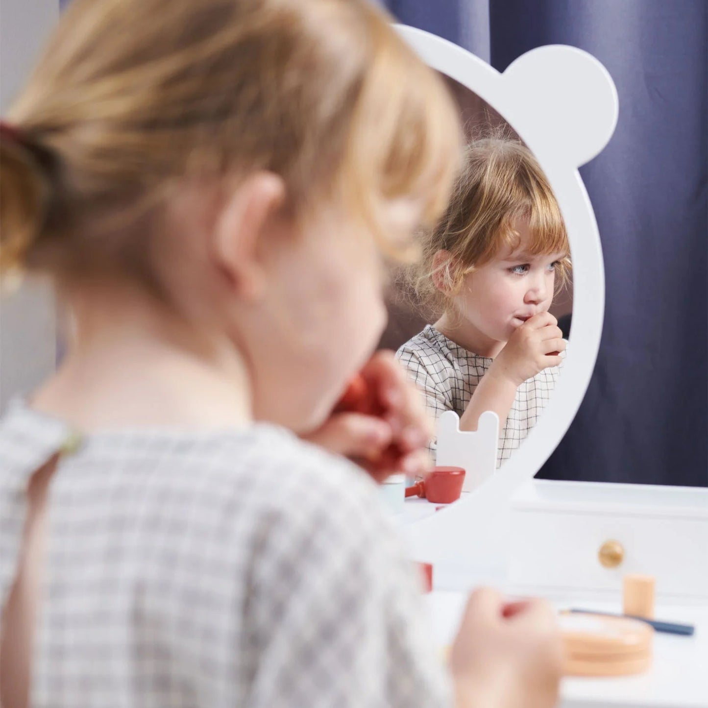 Child looking at themselves in a mirror with a vanity table.