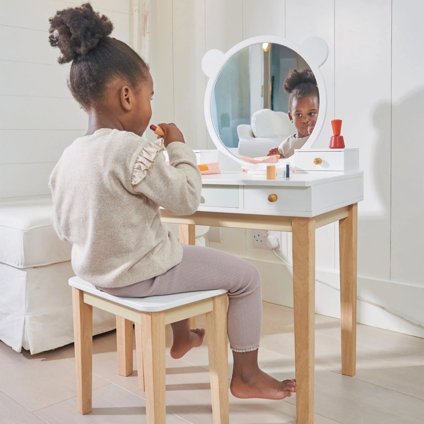 Child sitting at a small vanity table with a mirror, surrounded by children's products.