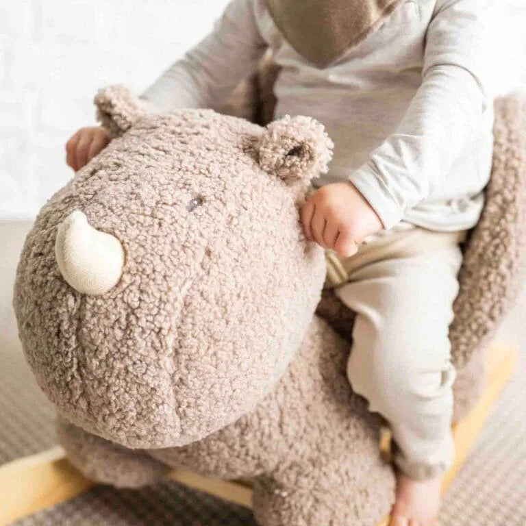 Child holding a plush rhino toy on a soft surface