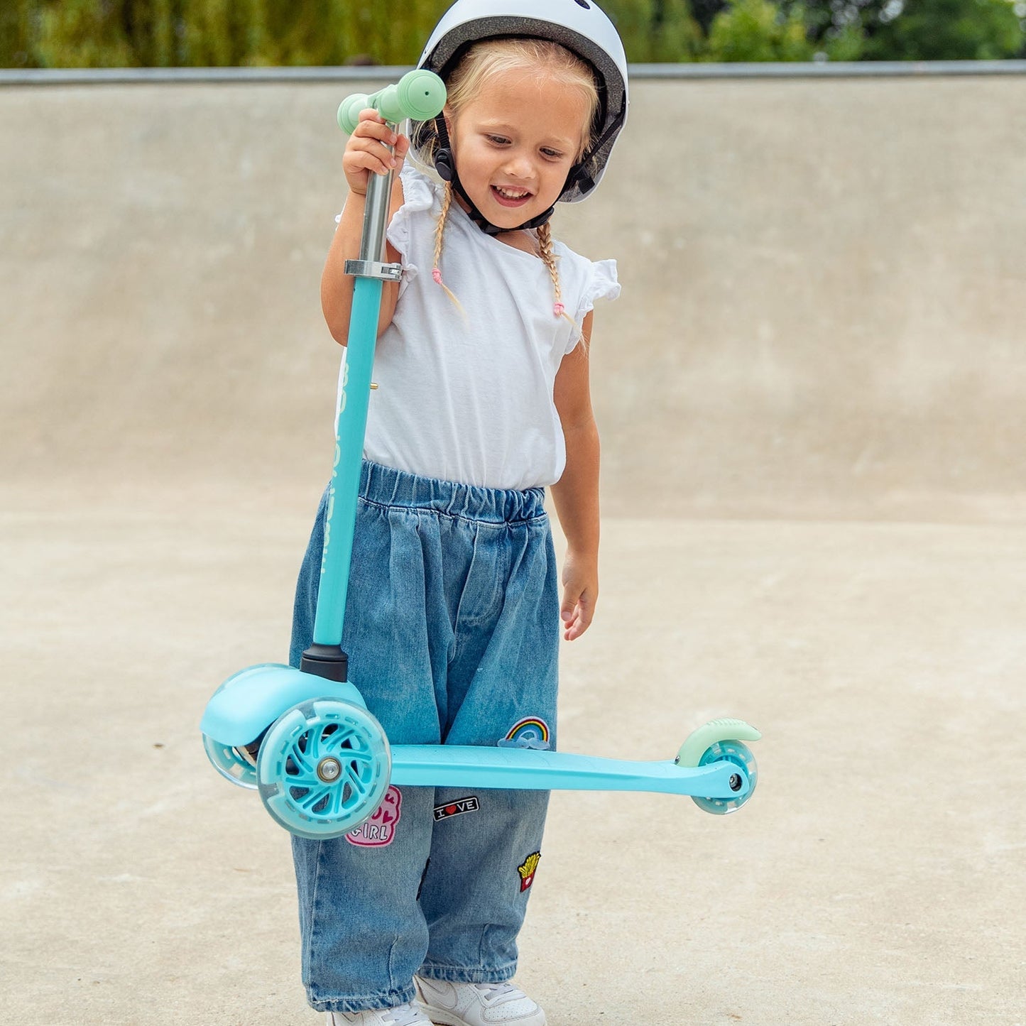 Child holding a blue scooter at a skate park