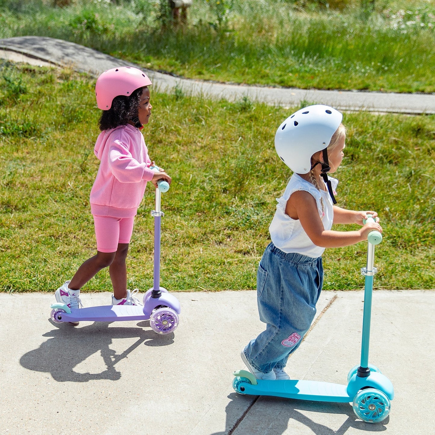 Two children on scooters wearing helmets in a park setting
