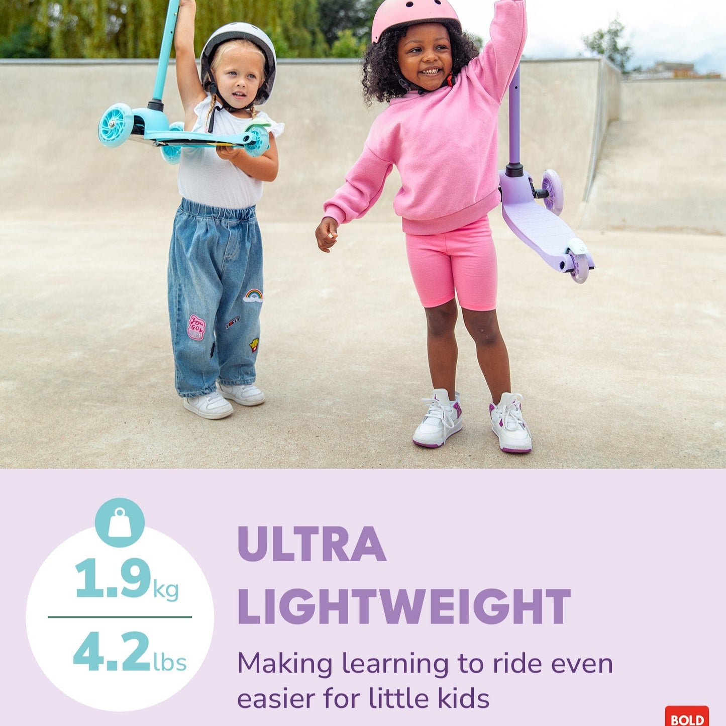 Two children with scooters on a concrete surface with a tree in the background.