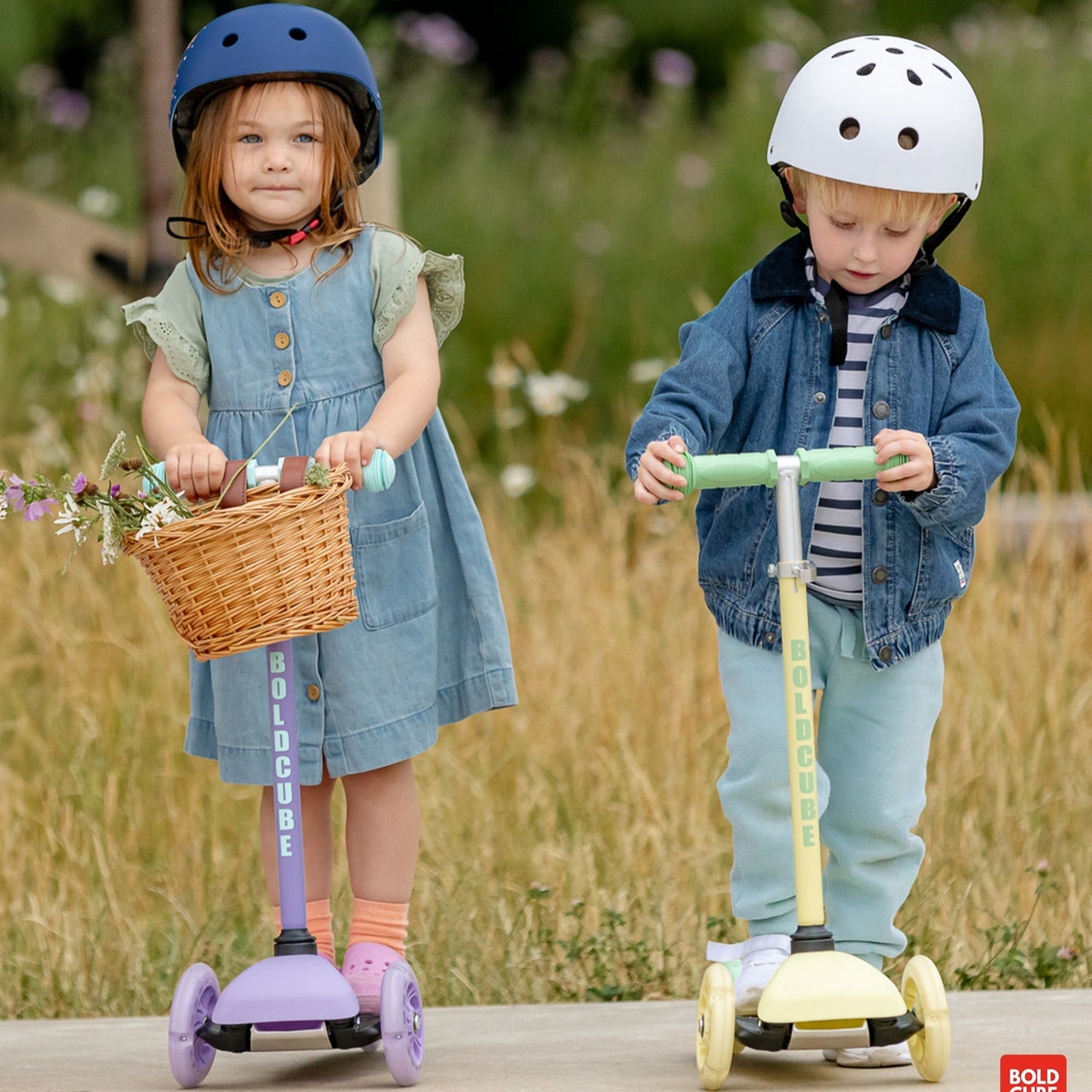 Two children on scooters with helmets in a natural setting