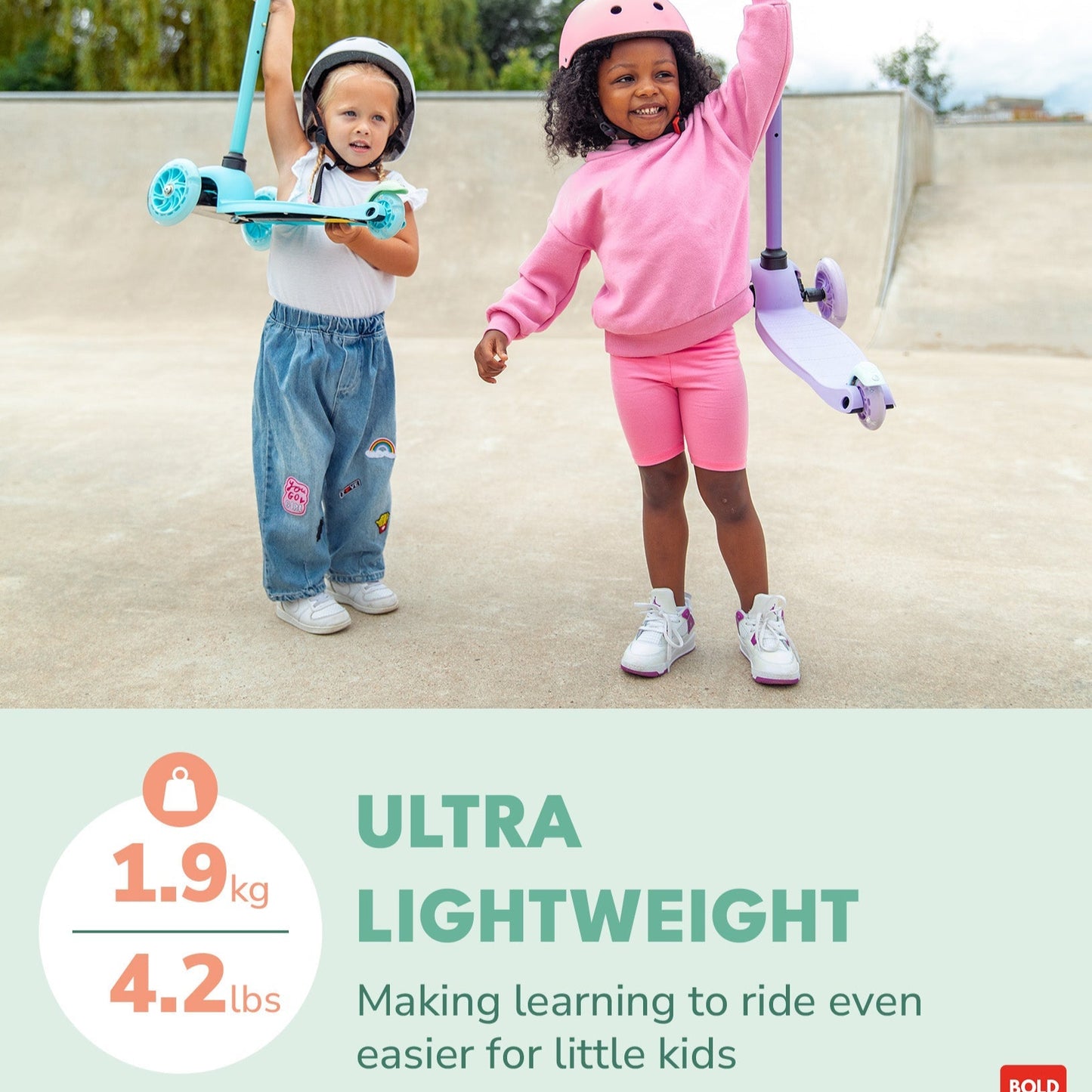 Two children with scooters and helmets on a concrete surface with trees in the background.