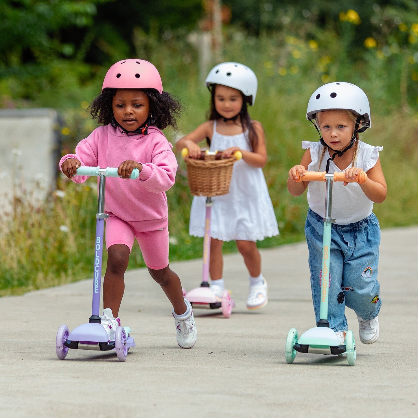 Three children on scooters with helmets in a park setting