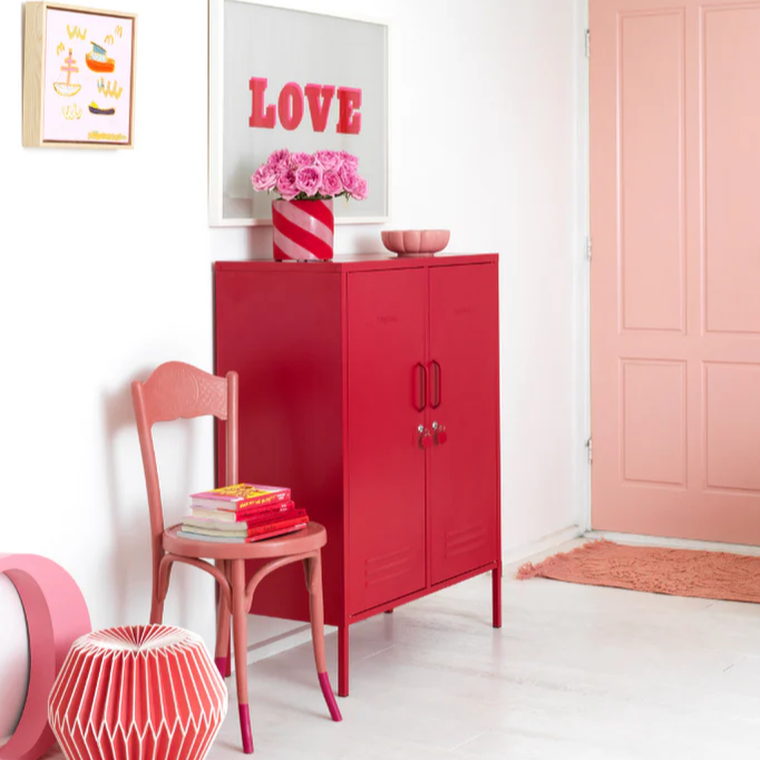 Modern interior with a red cabinet, pink chair, and decorative elements.