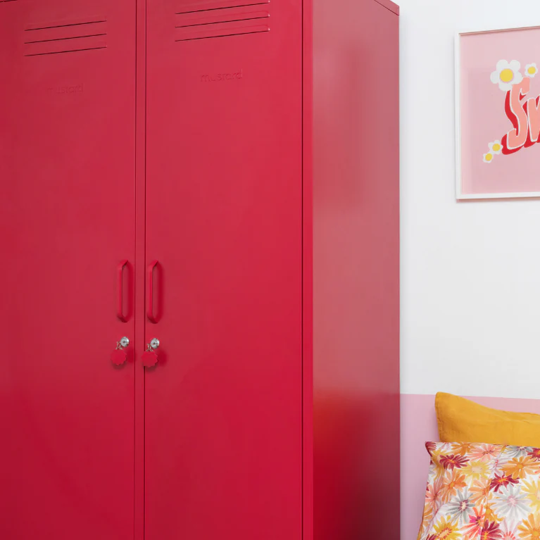Red locker next to a bed with floral bedding and yellow pillows, with a pink framed picture on the wall.