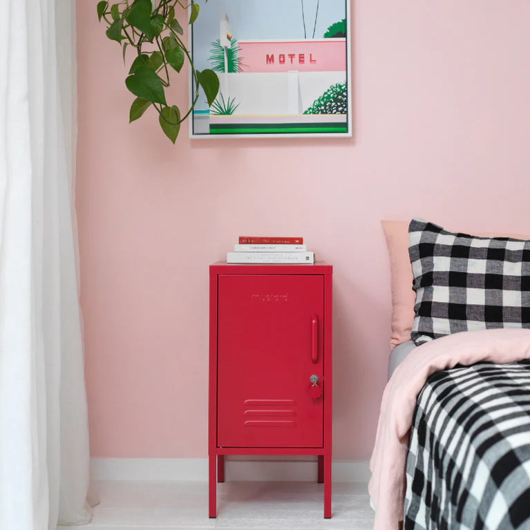 Red locker against a pink wall with a framed picture and a bed with checkered bedding.
