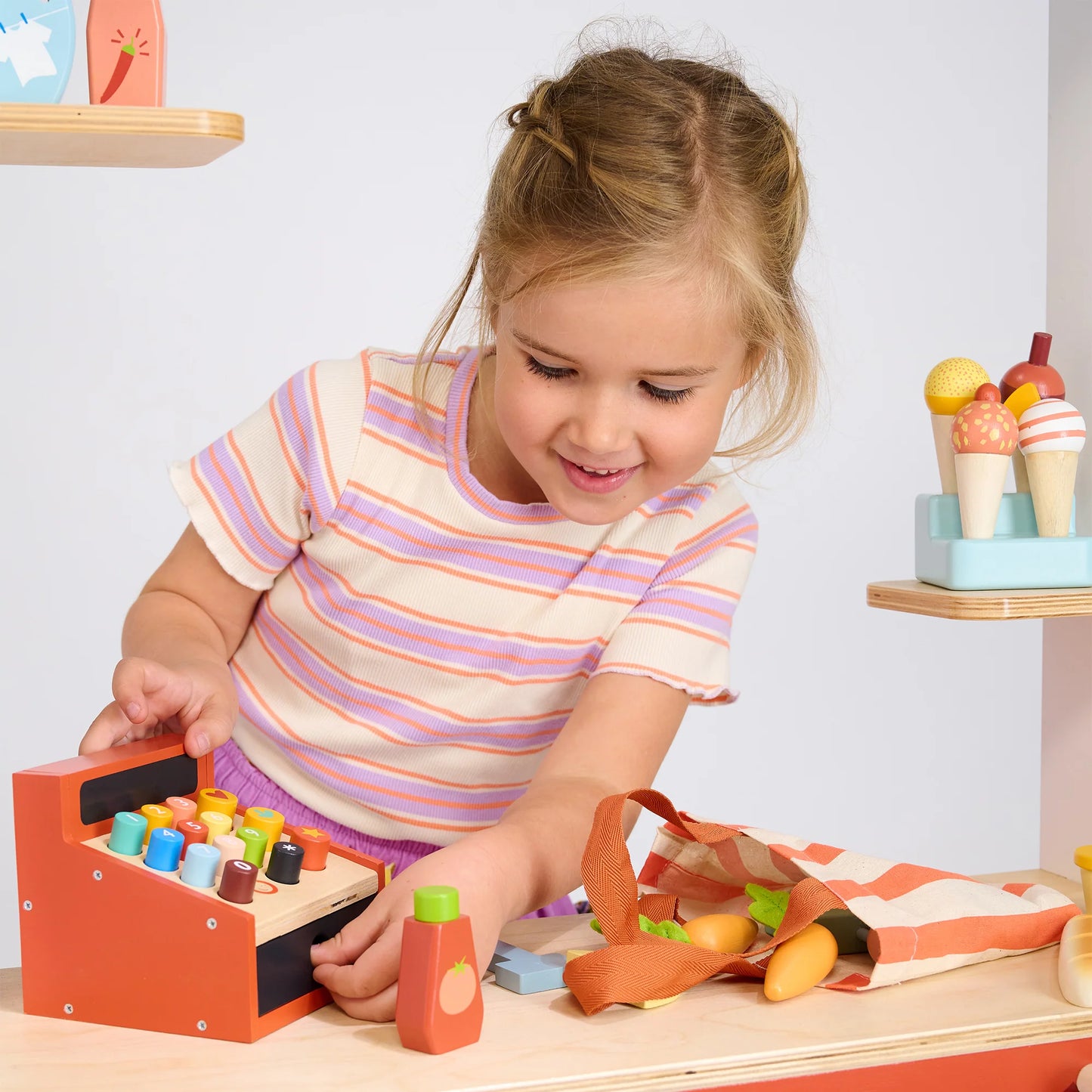 Child playing with a wooden toy cash register and blocks on a table.