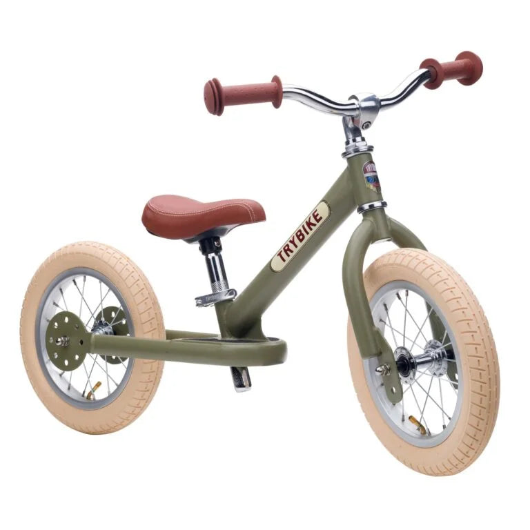 Children's balance bike with olive green frame and brown seat and handlebar tips on a white background