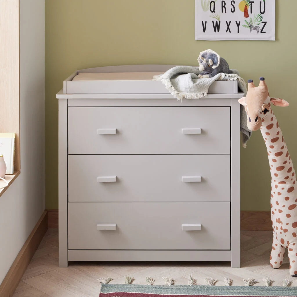 Gray dresser with changing table top in a nursery setting with toys and alphabet chart.