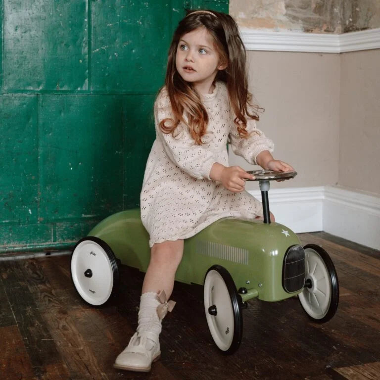 Young girl riding a green toy car indoors.