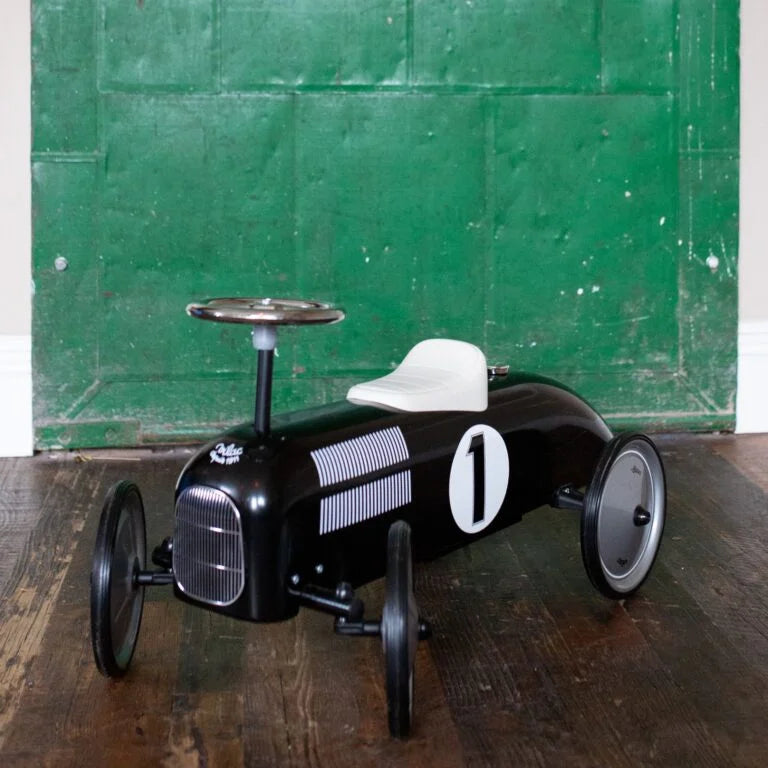 Black toy race car with number 1 on a wooden floor against a green wall.