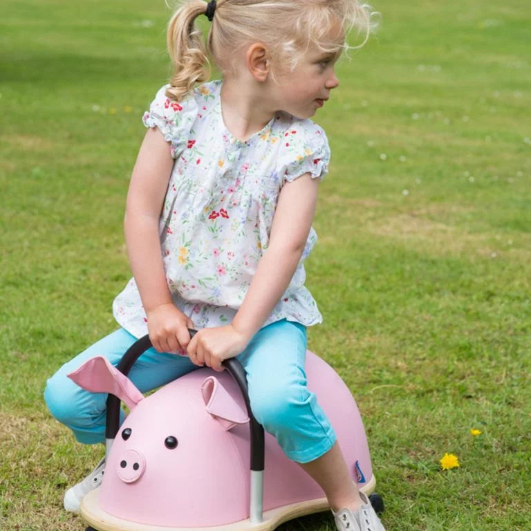 Young girl riding a pink toy horse on a grassy field