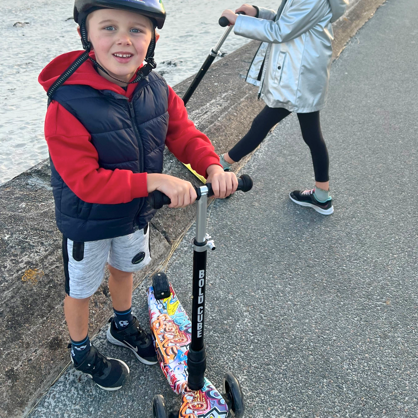 Child with a scooter on a sidewalk near a body of water