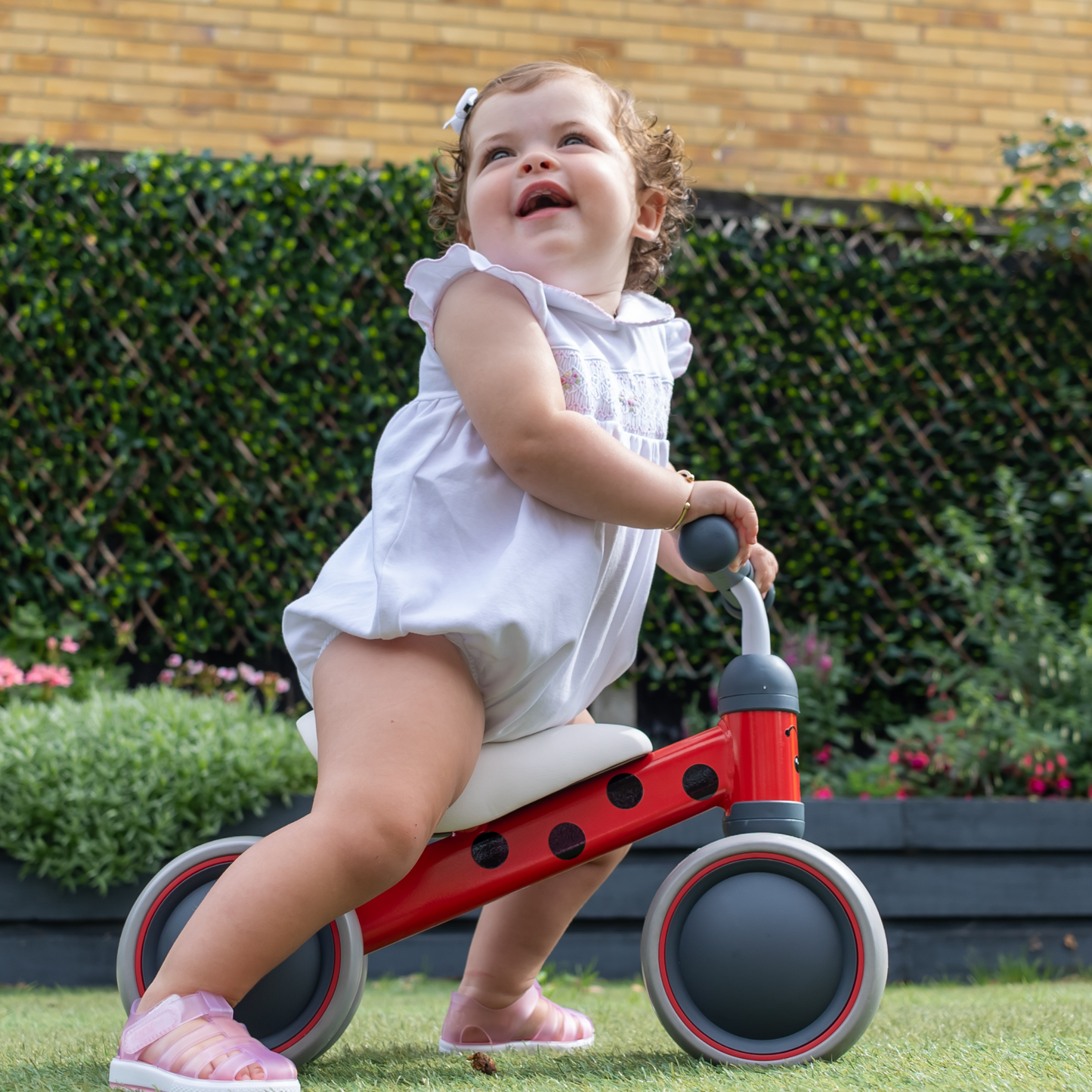 Child riding a red balance bike outdoors with greenery in the background