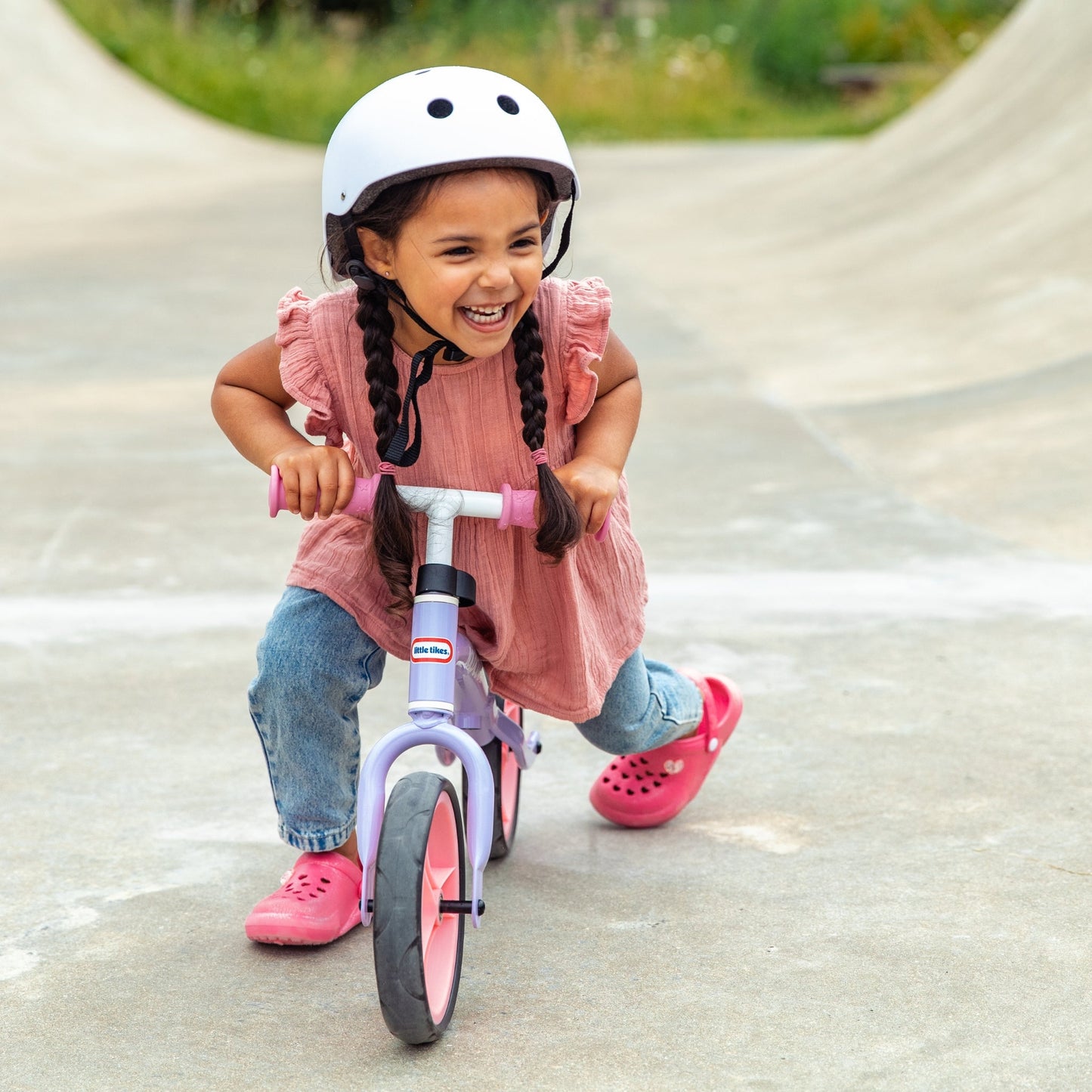 Child riding a balance bike with a helmet on a paved path