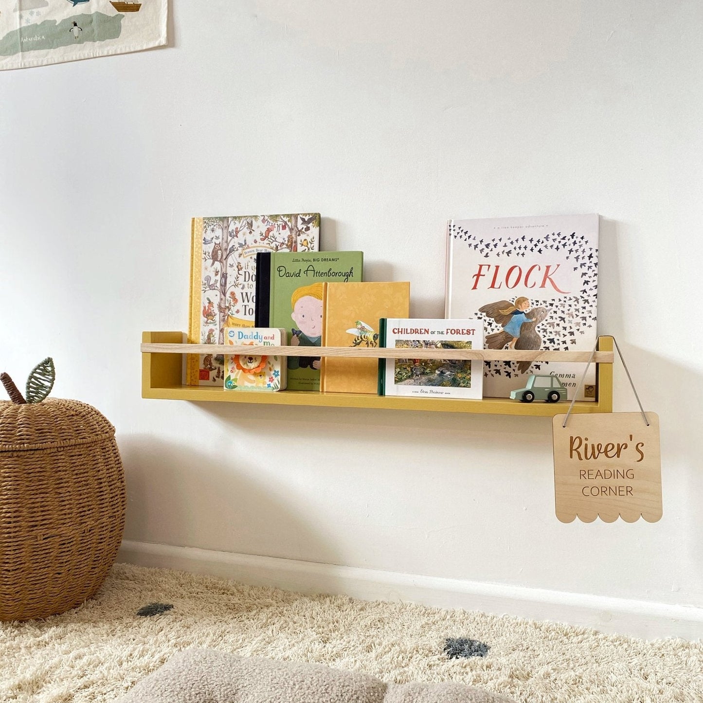 Yellow shelf with books and toys against a white wall, with a textured rug and wicker basket in the foreground.