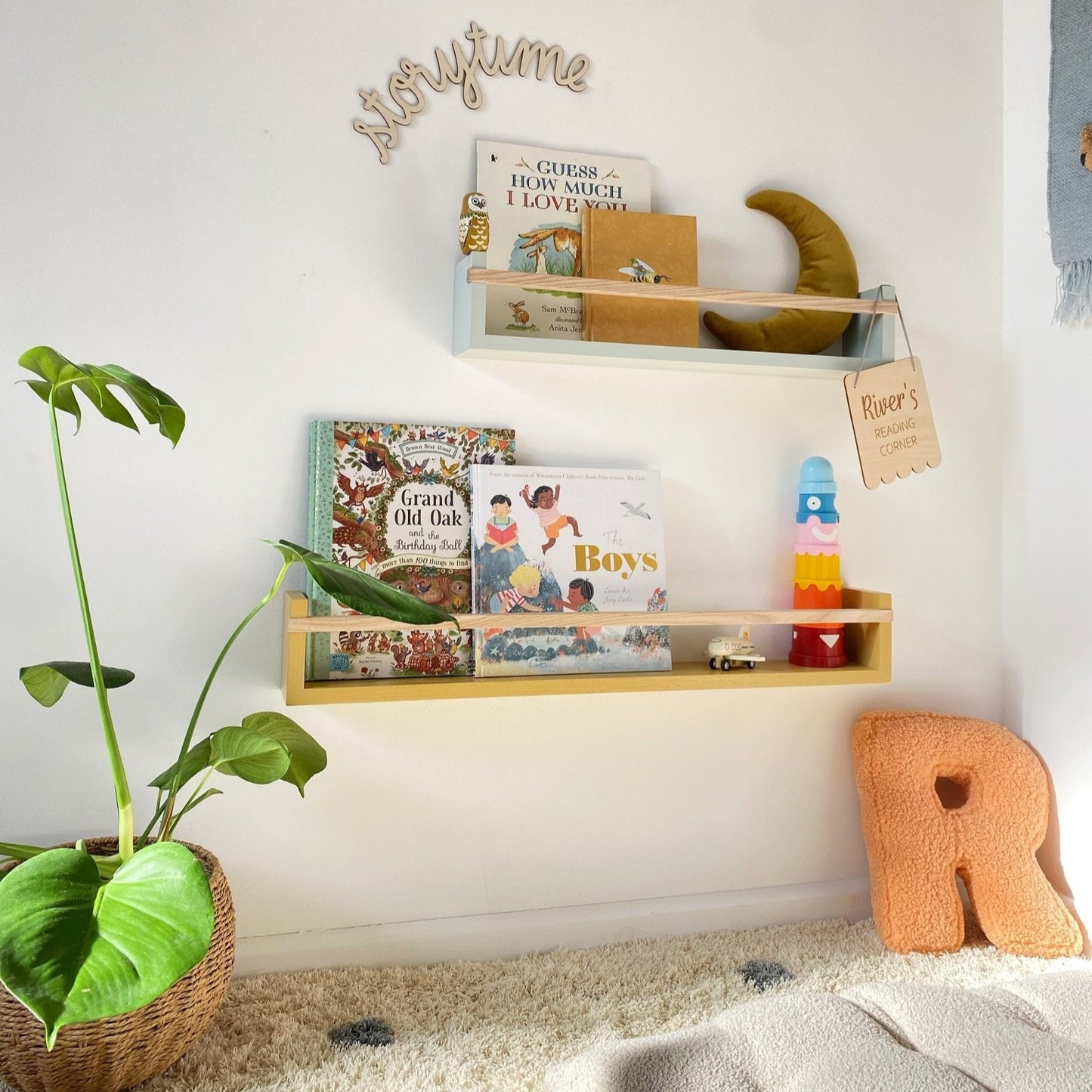 Children's room with a shelf displaying books and toys, a plant, and a decorative letter 'R'.