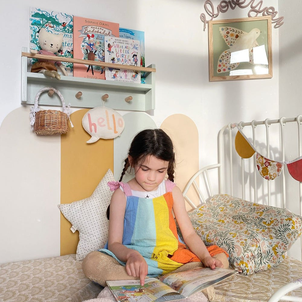 Child sitting on a bed reading a book in a cozy bedroom with decorative elements.