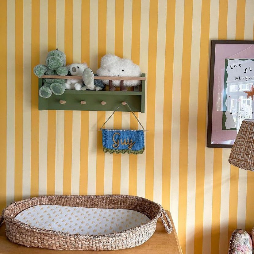 Children's room with yellow and white striped walls, a green shelf with toys, and a wicker basket on the floor.