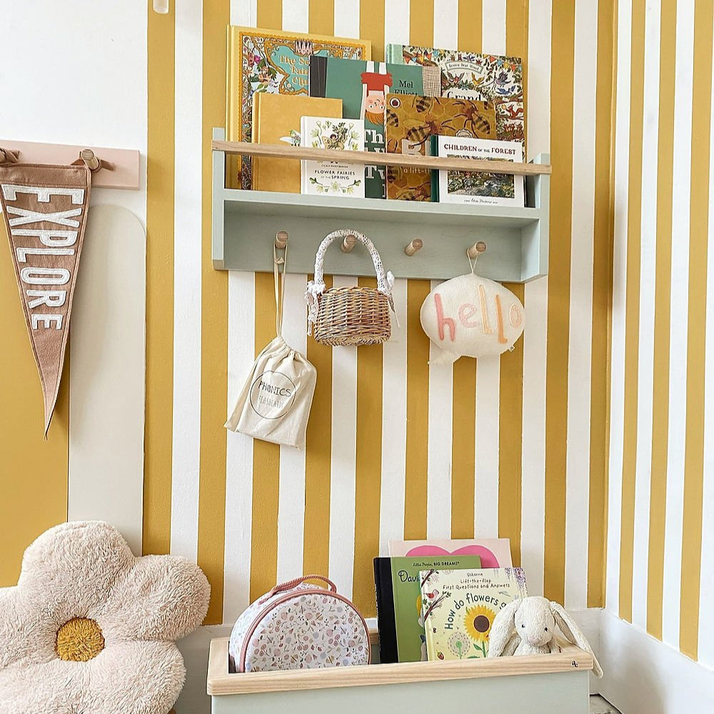 Children's room with a shelf, hooks, and decorative items against a yellow and white striped wall.