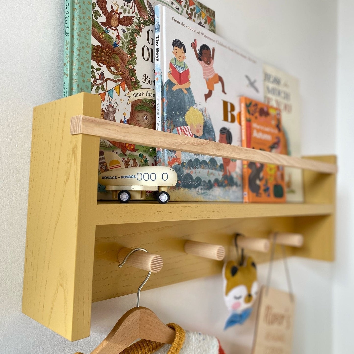 Wooden shelf with books, a toy car, and a hanger on a white wall.