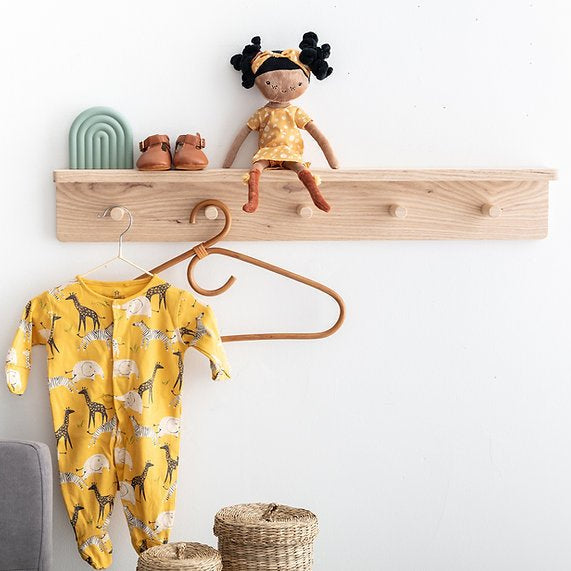 Yellow baby onesie with animal print hanging on a wooden shelf with a doll and shoes.