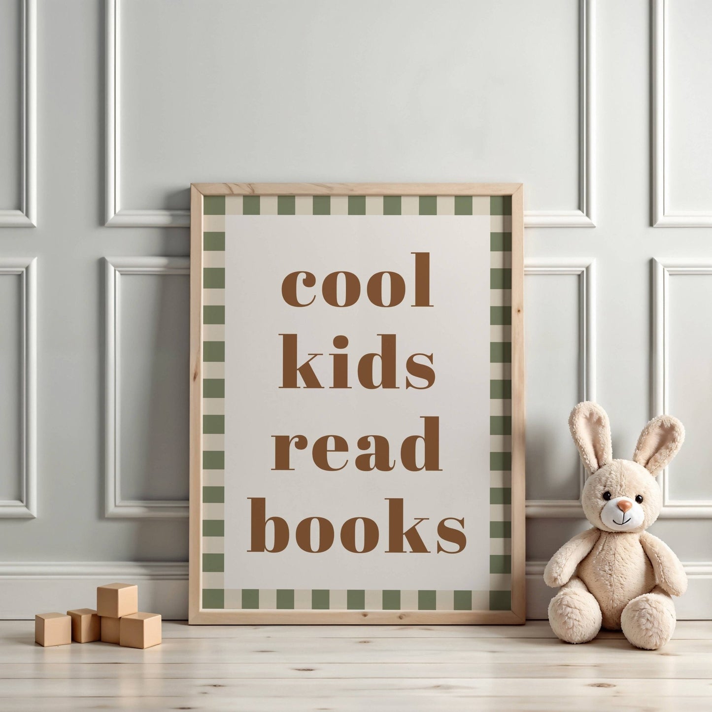 Framed poster with 'cool kids read books' text on a checkered background, placed on a wooden floor with a plush toy and blocks.