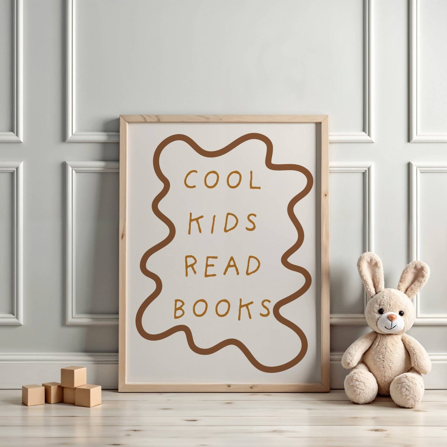 Framed poster with 'Cool kids read books' text on a wall with a teddy bear and wooden blocks.