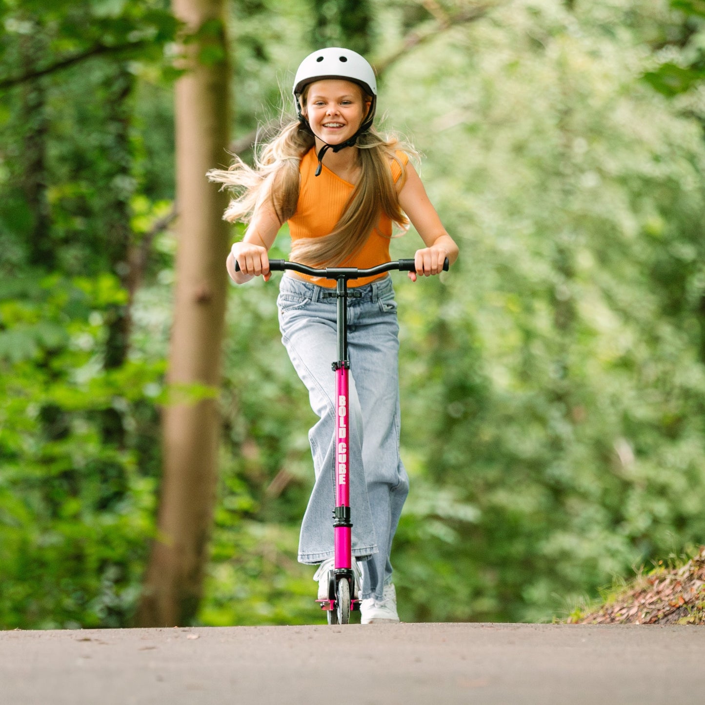 Young girl riding a pink scooter in a forested area