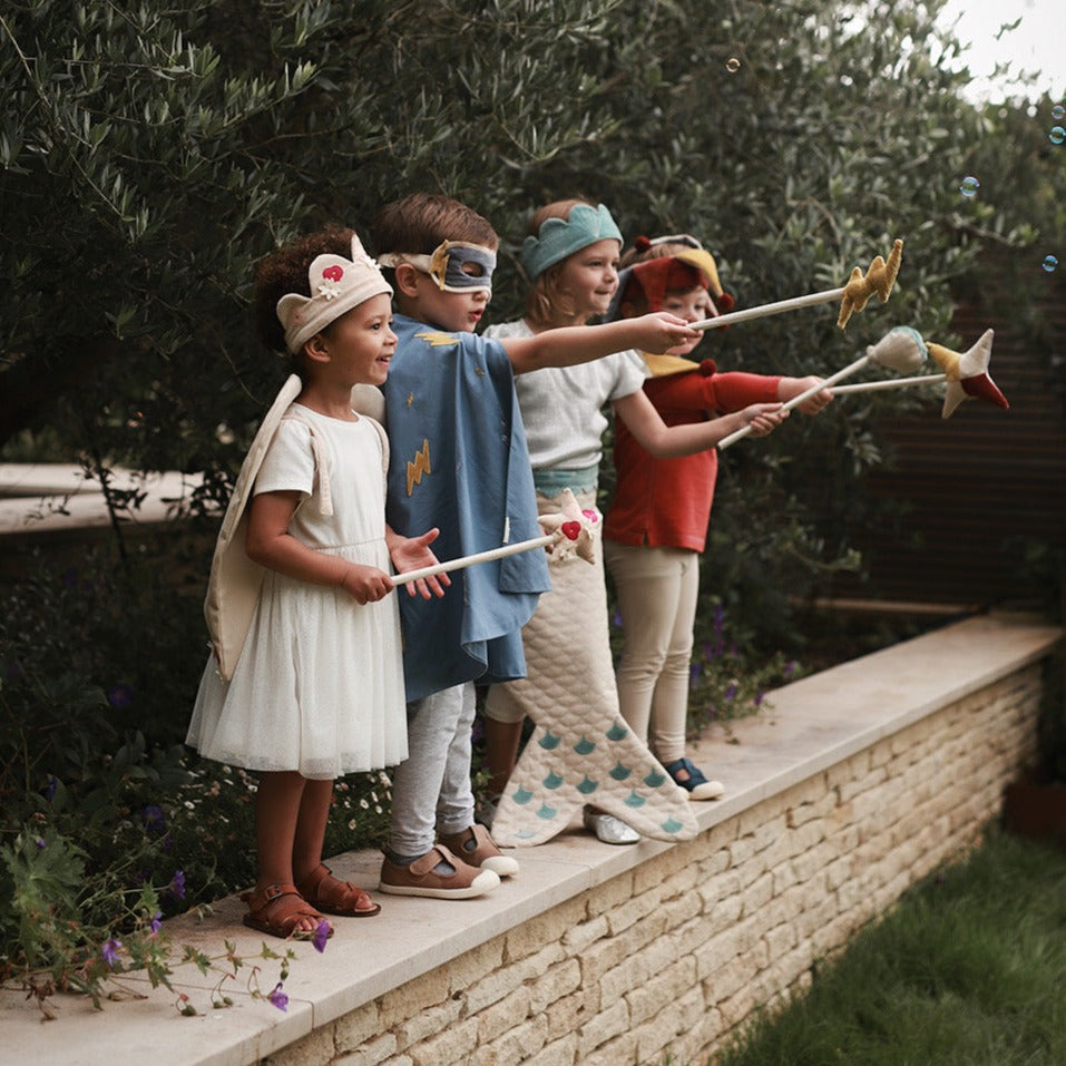 Children in costumes playing with toy bows and arrows outdoors.