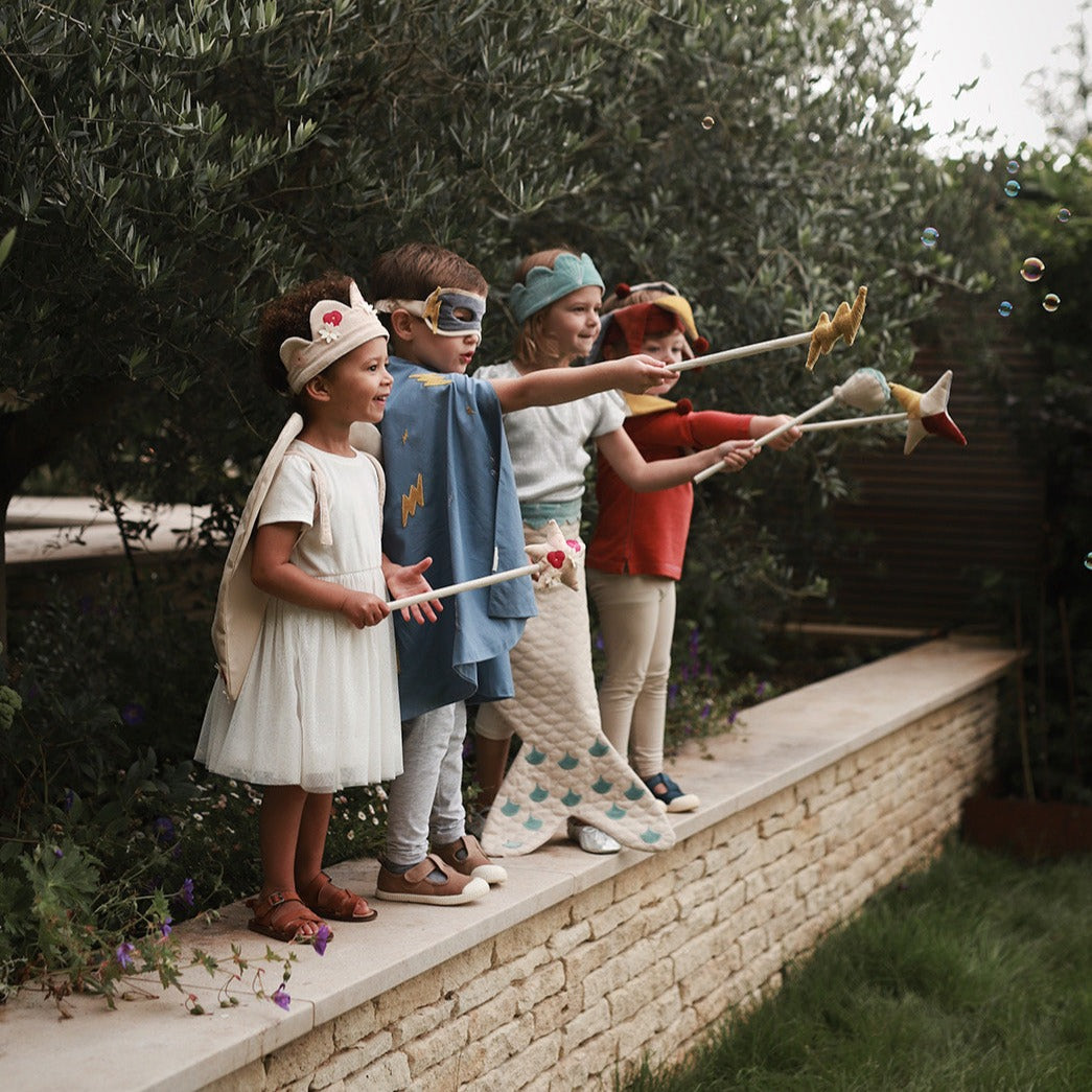 Children in costumes playing with bubble wands on a stone ledge outdoors.