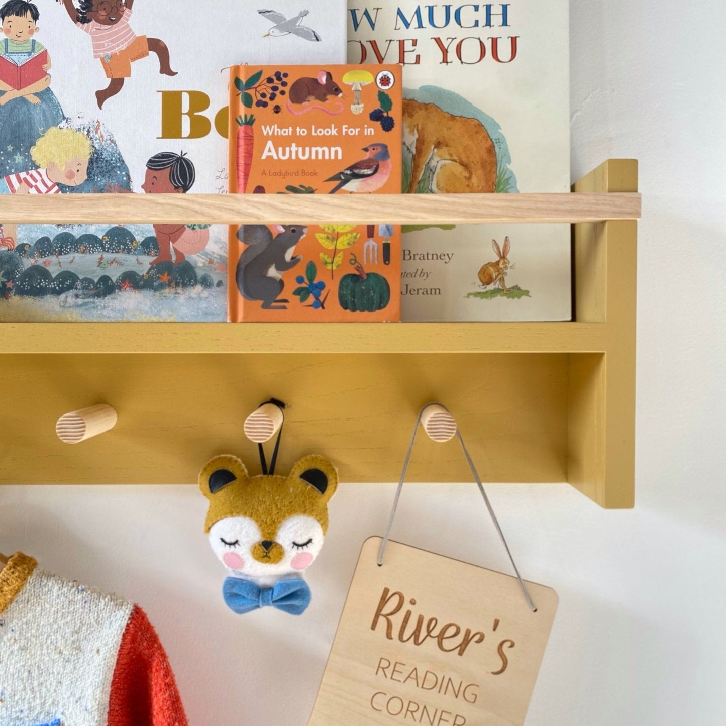 Wooden shelf with children's books and a sign indicating a reading corner, on a white wall.