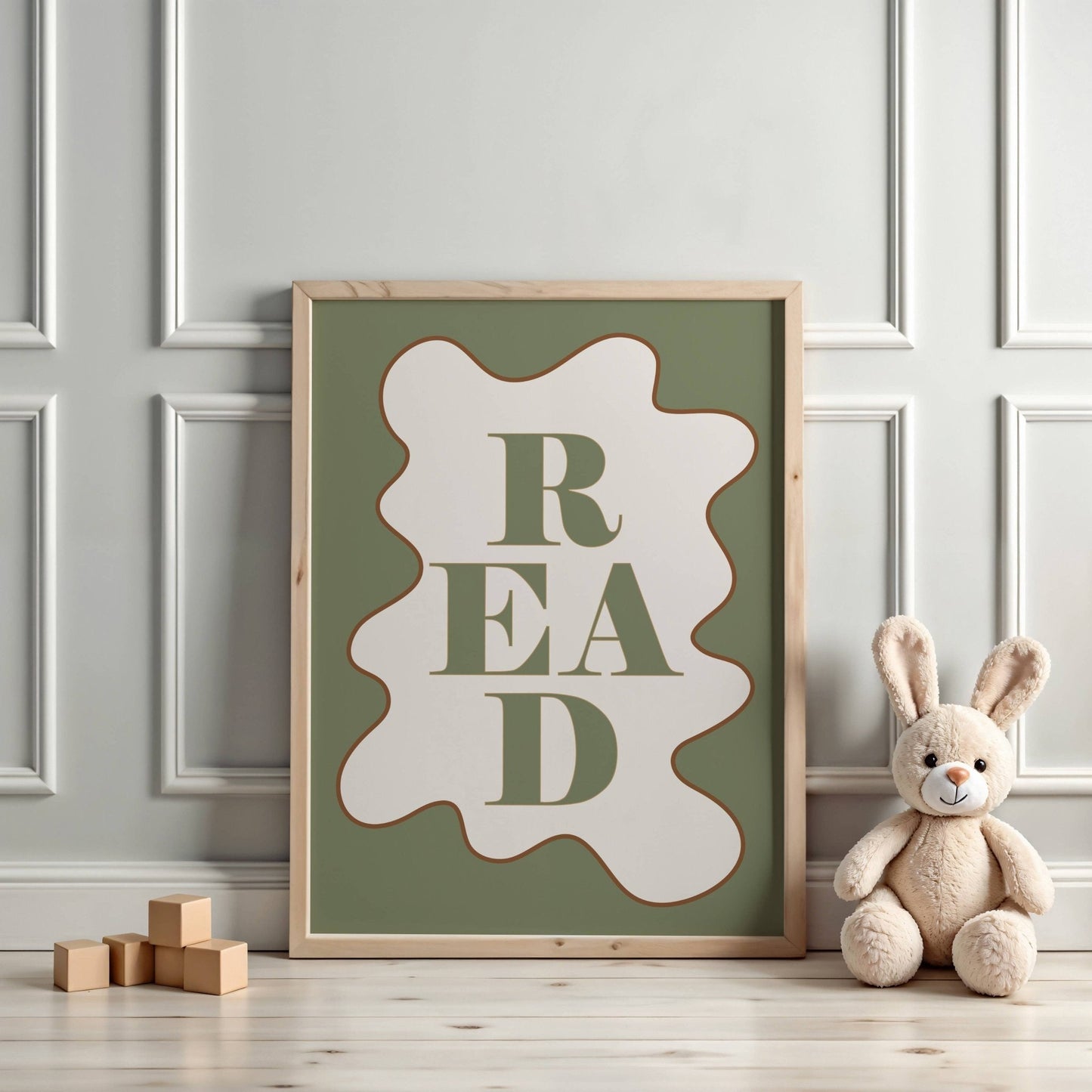 Framed poster with 'READ' text on a wall with a teddy bear and wooden blocks below.