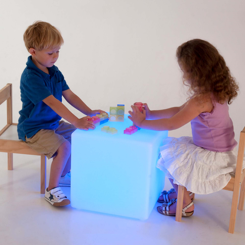 Two children playing with a glowing cube table on a white background