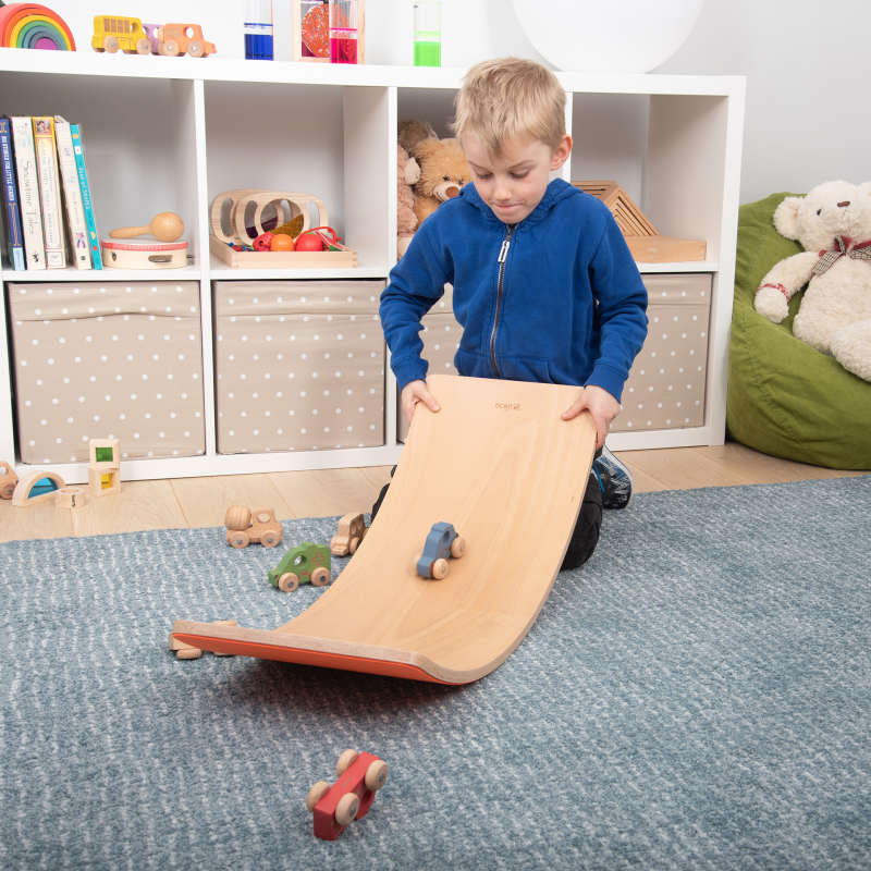 Child playing with a wooden board with toy cards in a room with shelves and toys.