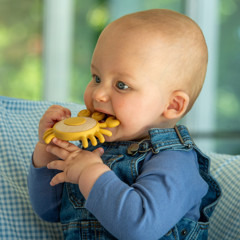 Baby playing with a yellow teething toy indoors