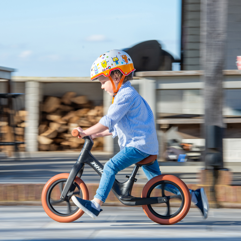 Child riding a balance bike with a colorful helmet on a street.