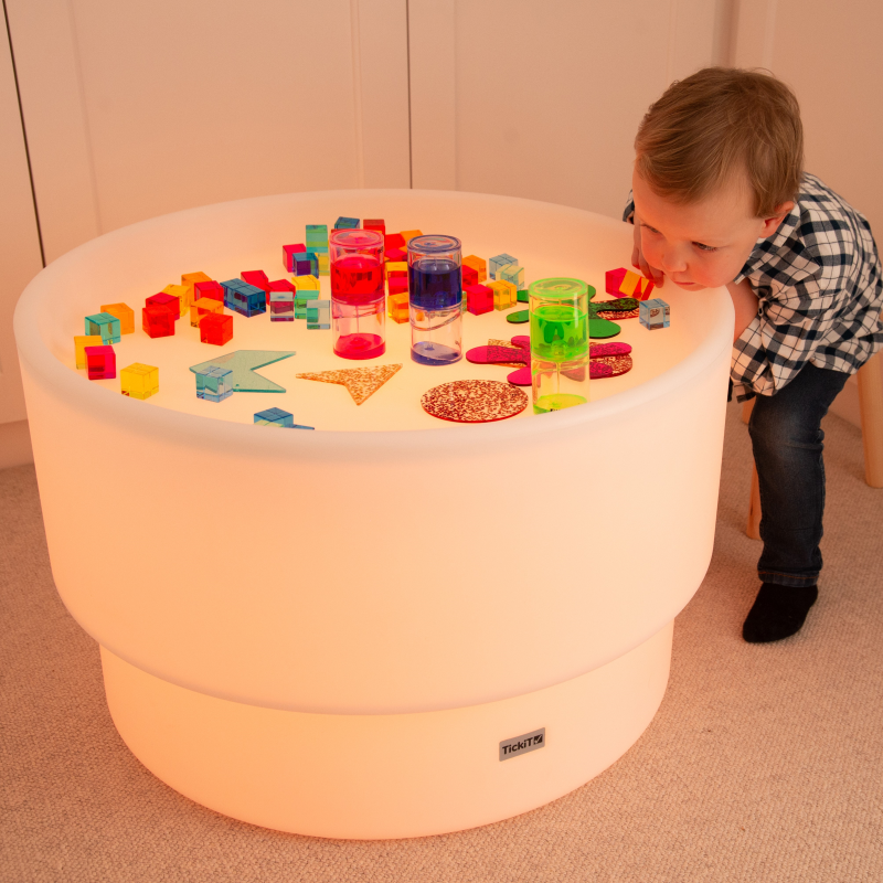 Child playing with colorful toys on a illuminated discovery table indoors.
