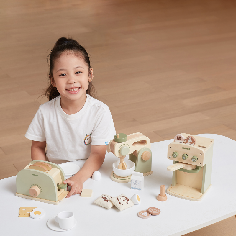 Child playing with a set of wooden food toys on a table, smiling at the camera.