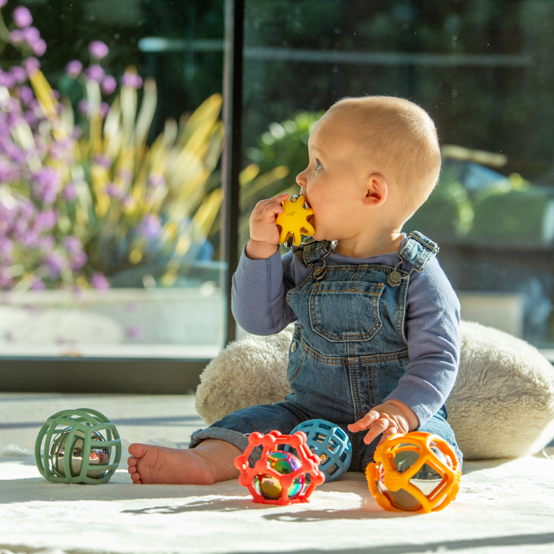 Baby playing with colourful grasping toys on a rug.