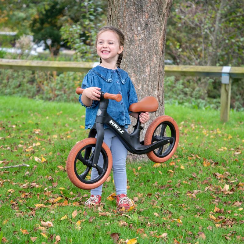 Child holding a balance bike outdoors near a tree