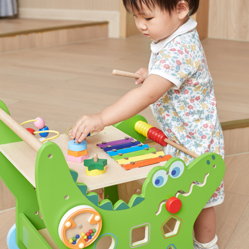Child playing with a colorful wooden walker on a wooden floor.