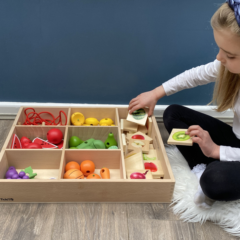 Child playing with a wooden toy set on a wooden floor.