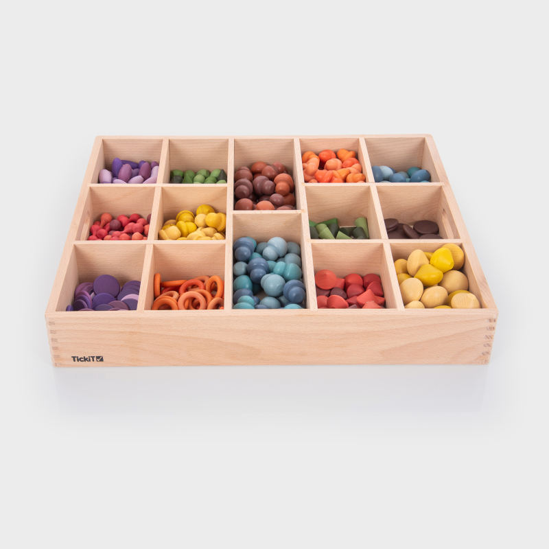 Wooden sorting toy with colourful loose parts in compartments on a white background